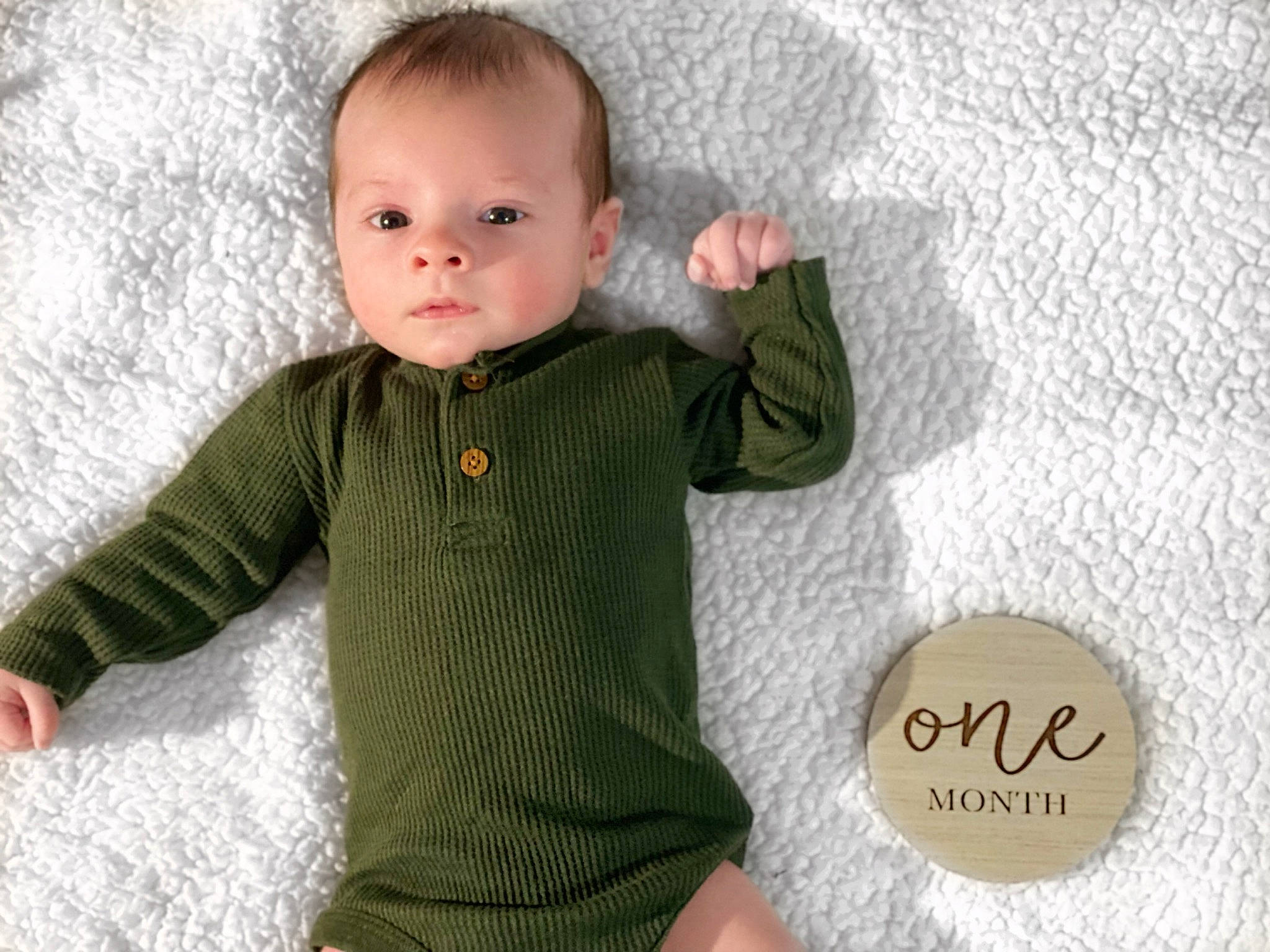 Noah is registered to the contest to win money with this photo: baby, baby_toddler_clothing, cheek, child, comfort, finger, gesture, happy, linens, outerwear, pattern, person, product, skin, sleeve, t_shirt, textile, toddler, wood, wool