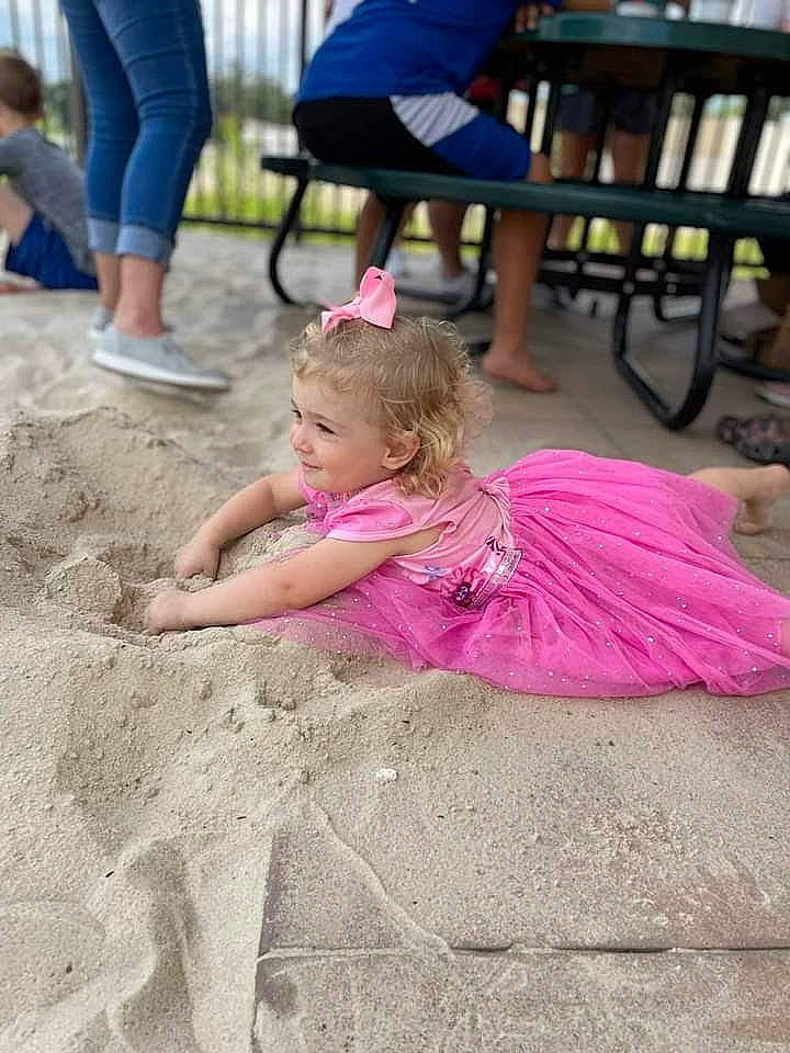 Kaydence is registered to the contest to win money with this photo: chair, child, event, fun, grass, happy, leg, leisure, magenta, person, pink, play, recreation, sand, shorts, sitting, soil, summer, table, toddler