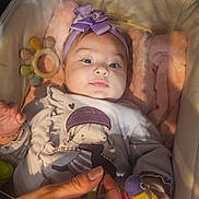 Alaya Pereira Berrio a rejoint le concours — aidez-le/la à gagner de superbes lots ! baby, infant, headband, bow, toy, bird_toy, bassinet, blanket, cushion, hand, clothing, purple, cute, child, portrait, indoor, soft_lighting, smile, person, closeup