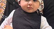 Isaac joined the competition — help win amazing prizes! adult, baby, beanie, bib, black_bib, child, closeup, clothing, cute, expression, face, hand, holding, infant, outdoor, patterned_strap, person, portrait, tattoo, white_shirt