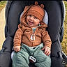baby, child, stroller, hoodie, bear_ears, green_pants, smiling, happy, outdoor, sidewalk, grass, cute, infant, clothing, casual_wear, portrait, seated, baby_face, playful, warm_clothes
