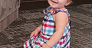 Meadow is registered to the contest to win money with this photo: child, toddler, baby, smiling, sitting, portrait, dress, checkered_dress, colorful_clothing, blonde_hair, blue_eyes, earring, carpet, indoor, floor, wall, door, happy, cute, photography