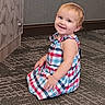 child, toddler, baby, smiling, sitting, portrait, dress, checkered_dress, colorful_clothing, blonde_hair, blue_eyes, earring, carpet, indoor, floor, wall, door, happy, cute, photography