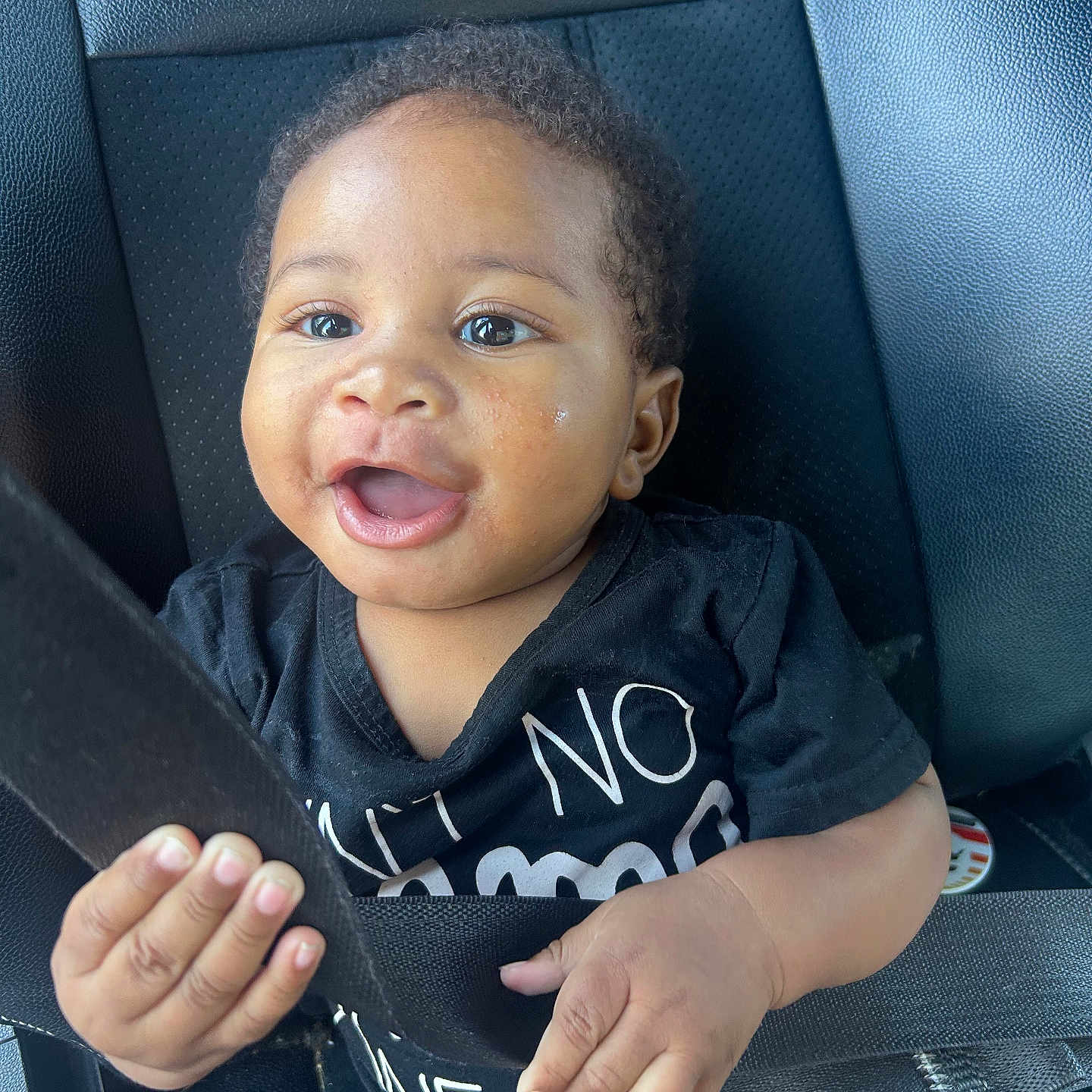 Caleb is registered to the contest to win money with this photo: baby, child, car_seat, seatbelt, black_shirt, blue_jeans, happy, smiling, hands, face, eyes, curly_hair, infant, sitting, indoors, car_interior, safety, cute, portrait, person