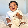 Rhian joined the competition — help win amazing prizes! baby, smiling, white_outfit, sneakers, bed, indoor, happy, portrait, child, cute, infant, person, young_child, curly_hair, buttoned_shirt, candid, seated, fist, joyful, bright