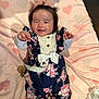 baby, infant, smiling, winking, floral_outfit, navy_blue, pink_blanket, hearts_pattern, lying_down, baby_toys, ruffles, cute, playful, child, indoors, soft_texture, headband, happy, person, portrait