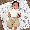 baby, child, smiling, blanket, bear_pattern, white_polo_shirt, beige_shorts, socks, carpet, happy, cute, infant, playful, lying_down, indoors, portrait, clothing, toddler, hands, face