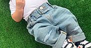 Jesus is registered to the contest to win money with this photo: baby, infant, child, grass, soccer_ball, footwear, sneakers, jeans, white_shirt, hat, outdoor, sports, cute, lying_down, toy, green_background, casual, relaxed, portrait, young