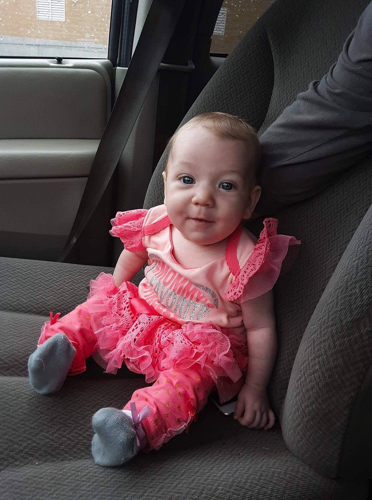 Elana is registered to the contest to win money with this photo: baby, beauty, car_seat, cheek, child, electronic_device, eye, face, finger, hand, head, leg, lip, mouth, person, pink, sitting, skin, smile, standing