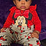 apparel, baby, black_socks, child, cozy, cute, expression, face, hands, indoors, minnie_mouse, patterned_pants, person, plush_background, portrait, purple_background, red_clothing, sitting, wide_eyes, young_child