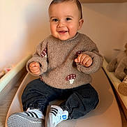 Gabin participe au concours pour gagner de l'argent avec cette photo : baby, child, smiling, sweater, mushroom_pattern, shoes, adidas, sneakers, pants, sitting, indoor, changing_pad, wooden_floor, toy, stuffed_animal, face, hands, happy, portrait, cozy