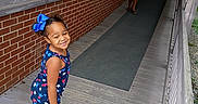 Damiana is registered to the contest to win money with this photo: child, children, smiling, outdoor, ramp, walkway, brick_wall, wooden_floor, railing, blue_bow, dress, shorts, sandals, portrait, siblings, standing, happy, residential_building, greenery, daylight