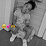child, toddler, portrait, sitting, pouting, curly_hair, smiling, sneakers, dress, backpack, porch, doorway, wooden_floor, wooden_wall, chair, box, black_and_white, emojis, outdoor, vintage_filter