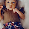 baby, infant, child, portrait, lying_down, indoor, blanket, bow, headband, dress, colorful_clothing, brown_shirt, patterned_skirt, wide_eyes, looking_at_camera, facial_expression, arms, legs, cozy, photography