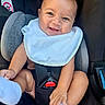 baby, smiling, car_seat, bib, happy, infant, child, cute, seatbelt, hands, feet, clothing, skin, person, safety, cute_expression, indoors, closeup, head, portrait