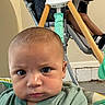 Noah is registered to the contest to win money with this photo: baby, child, cute, expression, family, floor, footwear, furniture, green_shirt, high_chair, indoor, infant, person, picture_frame, playful, portrait, reaching_hand, seat, serious_face, wall