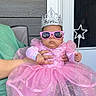 Aurora is registered to the contest to win money with this photo: baby, child, pink_dress, princess_costume, crown, sunglasses, star_wand, dress, sparkles, glitter, outdoor, patio, chair, door, window, adult_hand, portrait, costume, fashion, royalty