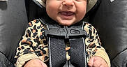 Aurora is registered to the contest to win money with this photo: baby, child, infant, smiling, car_seat, harness, hat, bear_hat, leopard_print, onesie, clothing, portrait, indoors, close_up, face, hands, safety_straps, blanket, vehicle, happy