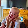 baby, smiling, bib, indoor, television, wooden_cabinet, adult, holding, happy, child, feet, face, person, clothing, furniture, living_room, joy, cute, infant, home