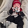 baby, infant, pacifier, hat, red_hat, blanket, clothing, orthopedic_shoes, footwear, black_pants, white_top, soft_texture, indoors, child, cute, lying_down, warm_clothing, baby_boy, face, small_hands