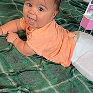 Thiago is registered to the contest to win money with this photo: baby, child, curious, cute, expression, face, floor, green_blanket, hair, happy, indoors, infant, lying_down, peach_shirt, person, plaid, playful, skin, smiling, white_pants
