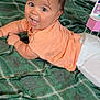baby, child, curious, cute, expression, face, floor, green_blanket, hair, happy, indoors, infant, lying_down, peach_shirt, person, plaid, playful, skin, smiling, white_pants