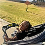 toddler, child, stroller, outdoor, park, grass, tree, sidewalk, smiling, sunlight, afternoon, sky, clouds, mountains, shoes, black_shirt, happy, person, nature, daytime