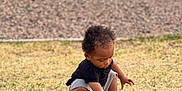 Kyree is registered to the contest to win money with this photo: toddler, child, grass, rock, sneakers, outdoor, curious, black_shirt, shorts, nature, daylight, playing, crouching, young_child, person, portrait, casual_clothing, exploring, field, sunny