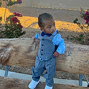 Kyree is registered to the contest to win money with this photo: toddler, child, bench, outdoor, vest, pants, shirt, bow_tie, white_shoes, curly_hair, tree, flowers, sunlight, daylight, looking_away, side_view, casual, nature, ground, wall