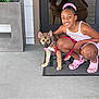 Luna is registered to the contest to win money with this photo: girl, dog, smiling, reflection, door, doormat, leash, crocs, hair_scrunchie, concrete, flower_pot, plant, outdoor, pet, young, happy, crouching, casual_clothing, summer, playful