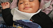 Iyahni-Rae is registered to the contest to win money with this photo: baby, infant, sleeping, smiling, portrait, face, child, blanket, cushion, seat, indoor, cozy, relaxed, black_clothing, bib, pink_fabric, blue_blanket, hand, nursery, photography