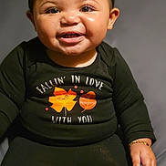 Iyahni-Rae joined the competition — help win amazing prizes! baby, child, smiling, portrait, sitting, indoors, black_clothing, long_sleeves, earrings, bracelet, happy, teeth, face, eyes, dark_background, studio_lighting, close_up, leaf_pattern, fall_fashion, ai_generated
