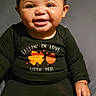 baby, child, smiling, portrait, sitting, indoors, black_clothing, long_sleeves, earrings, bracelet, happy, teeth, face, eyes, dark_background, studio_lighting, close_up, leaf_pattern, fall_fashion, ai_generated