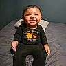 baby, child, infant, smiling, happy, portrait, sitting, bed, bedroom, pillow, black_clothing, onesie, long_sleeves, dark_hair, brown_eyes, hands, bracelet, indoor, photography, ai_generated
