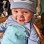 baby, child, smiling, blue_hat, clothing, indoor, person, hand, toy, furniture, floor, skin, face, eyes, mouth, happy, cute, infant, apparel, holding