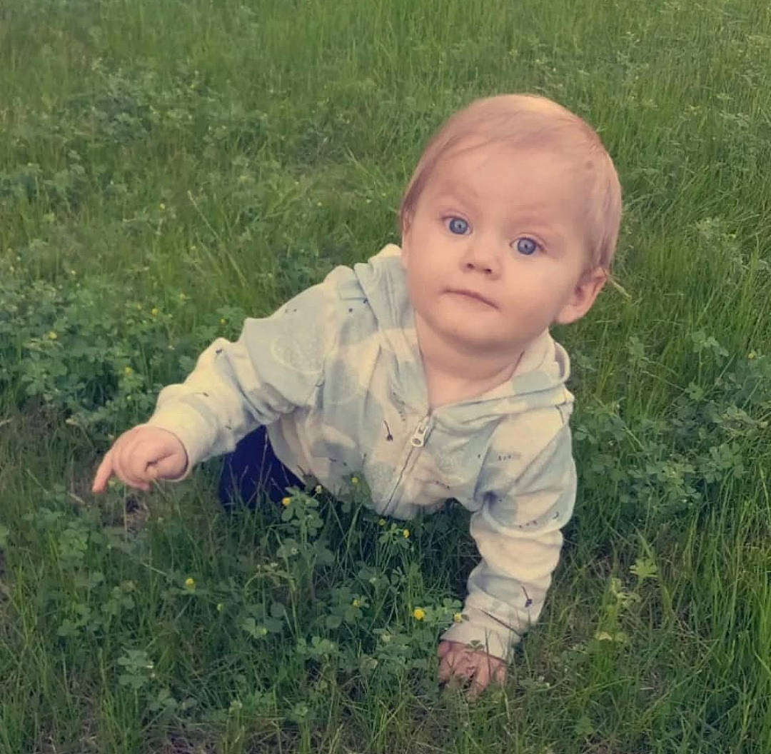 Braeson is registered to the contest to win money with this photo: baby, baby_toddler_clothing, eye, face, facial_expression, flooring, grass, grass_family, grassland, happy, head, lawn, meadow, natural_environment, nose, people_in_nature, person, plant, smile, standing