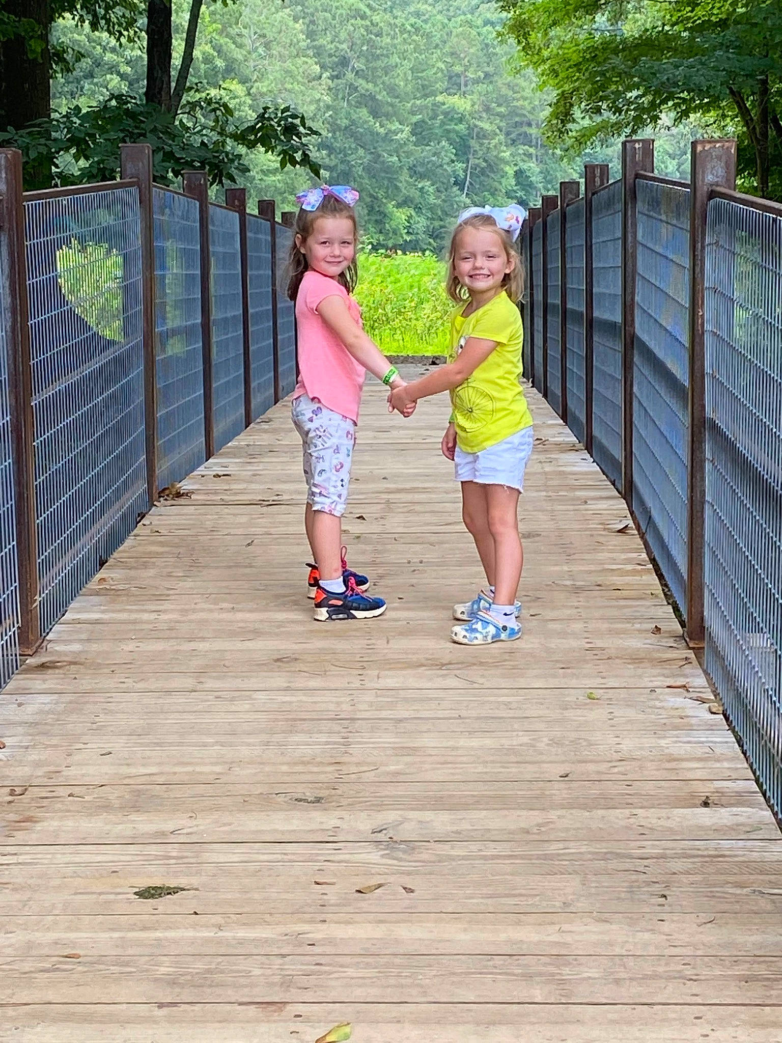 Leeana is registered to the contest to win money with this photo: boardwalk, deck, fence, fun, gesture, grass, happy, hardwood, holding_hands, joy, landscape, leg, leisure, people_in_nature, person, plant, recreation, shorts, toddler, tree