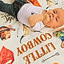 Ryker is registered to the contest to win money with this photo: baby, blanket, child, colorful, cowboy, curious, cute, face, hand, head, indoor, infant, jeans, lying_down, patterned_blanket, person, resting, skin, white_shirt, young_child