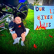 Ryker is registered to the contest to win money with this photo: baby, infant, motorcycle, black_clothing, grass, outdoor, sign, handmade_sign, text, harley_davidson, socks, chrome, reflection, tree, person, two_months, cute, child, motorbike, greenery