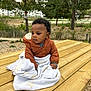baby, child, outdoor, picnic_table, blanket, jacket, wood, nature, tree, greenery, park, fence, curly_hair, infant, seated, daylight, casual_clothing, expression, young, fall
