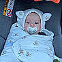 baby, pacifier, blanket, car_seat, hood, ears, face, infant, child, sitting, cute, wrapped, fabric, pattern, safety, warning_sign, indoor, comfort, calm, closeup
