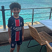 Zayn a rejoint le concours — aidez-le/la à gagner de superbes lots ! child, boy, smiling, sportswear, shorts, sneakers, curly_hair, waterfront, ocean, railing, cityscape, buildings, outdoor, daylight, patio, chair, table, grass_carpet, happy, person