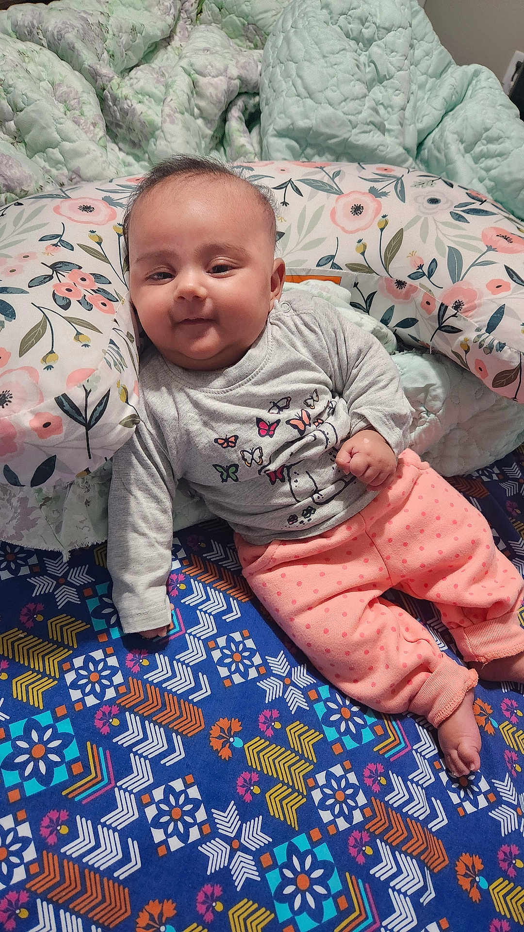 Zaynab joined the competition — help win amazing prizes! baby, blanket, butterfly_design, child, clothing, cozy, cute, floor, floral_pattern, indoors, infant, long_sleeve_shirt, patterned_blanket, person, pillow, polka_dot_pants, quilt, relaxed, smiling, soft_lighting
