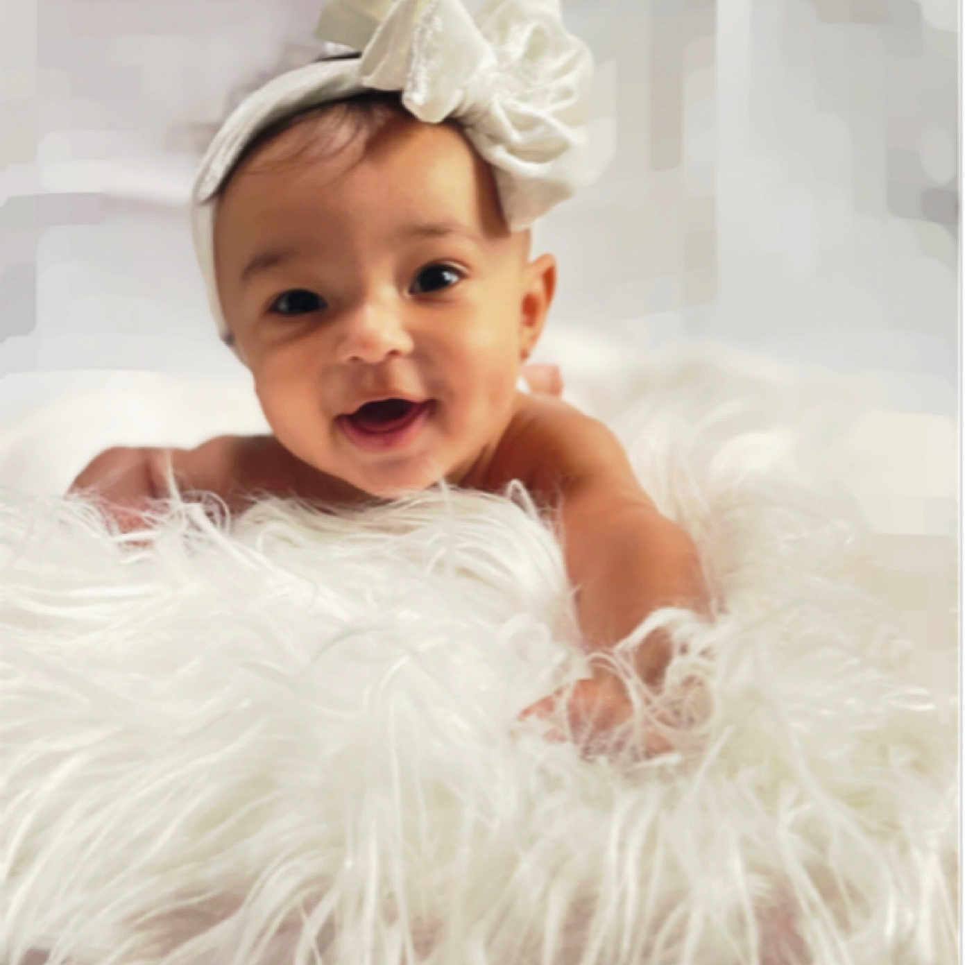 Irie joined the competition — help win amazing prizes! adorable, baby, child, closeup, cute, expression, face, fluffy_blanket, happy, headband, indoors, infant, portrait, reaching_hand, skin, smiling, soft_light, soft_texture, white_bow, young