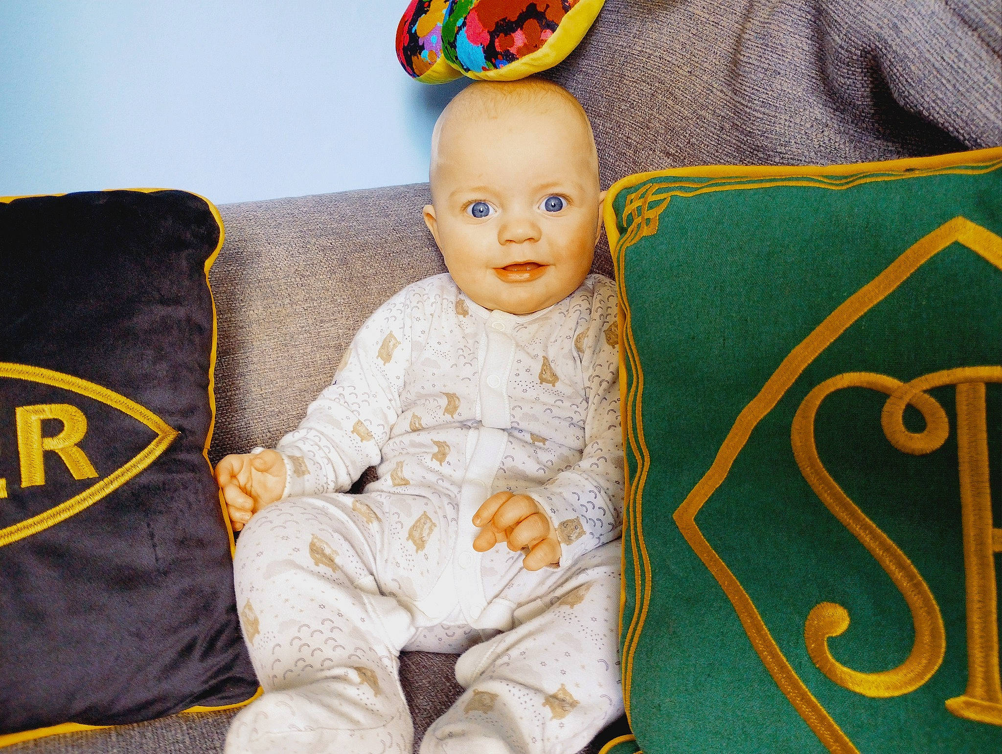 George is registered to the contest to win money with this photo: baby, baby_products, baby_toddler_clothing, baby_toys, child, comfort, couch, fashion_accessory, happy, linens, person, product, room, sitting, sleeve, smile, textile, throw_pillow, toddler, toy