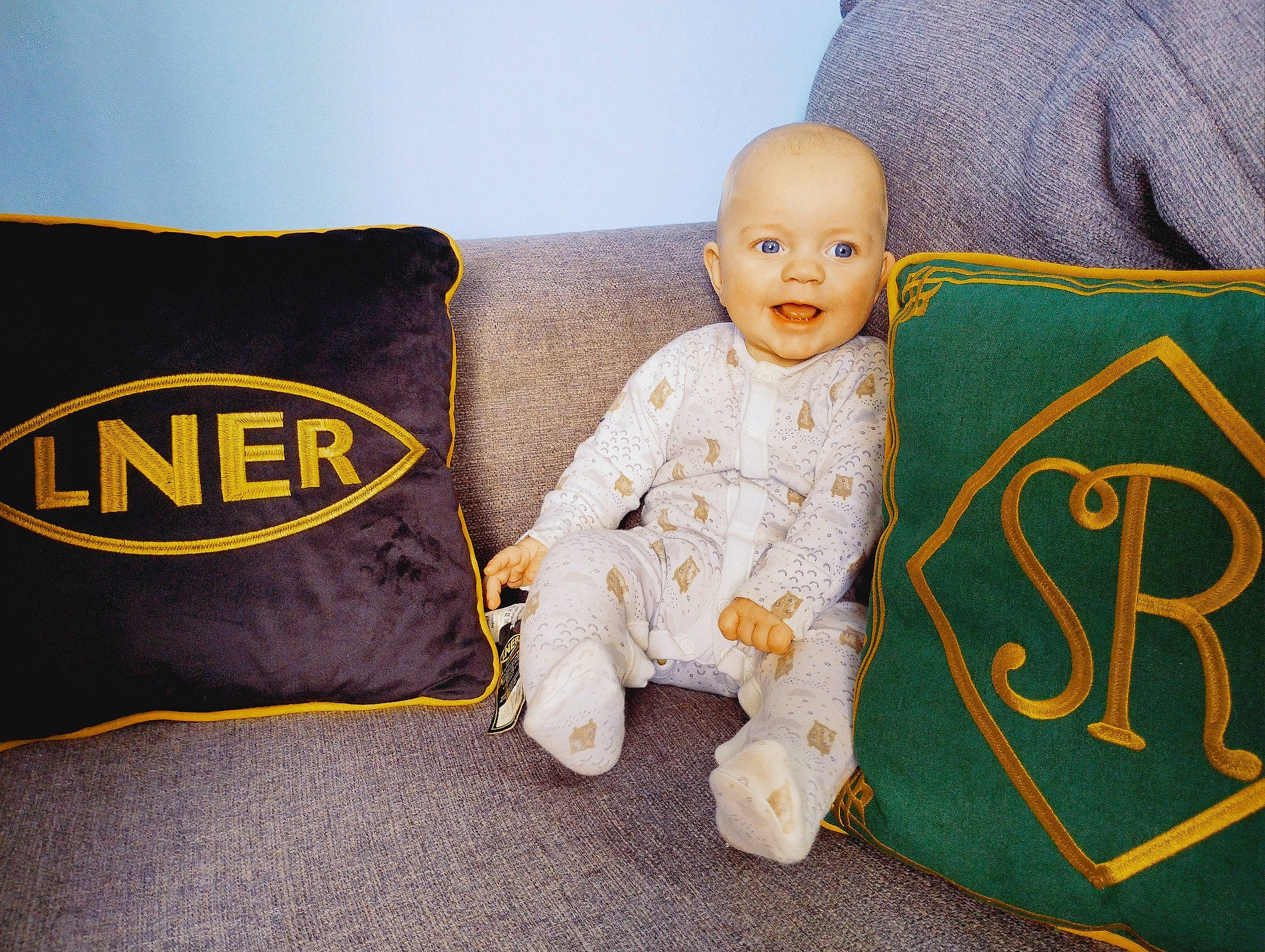 George joined the competition — help win amazing prizes! baby, baby_toddler_clothing, bedding, child, comfort, couch, flooring, font, happy, linens, logo, person, pillow, rectangle, room, sitting, sleeve, smile, t_shirt, throw_pillow