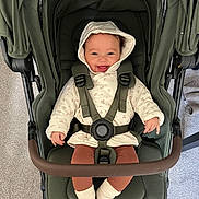 Ariella is registered to the contest to win money with this photo: baby, stroller, child, smile, hood, seatbelt, socks, happy, indoor, carpet, brown_pants, jacket, child_seat, infant, person, baby_clothing, footwear, baby_smiling, baby_in_stroller, baby_sitting