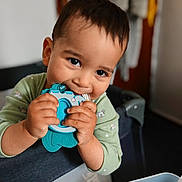 Kevin joined the competition — help win amazing prizes! toddler, child, toy, teething_toy, indoor, playpen, smiling, cute, baby, person, clothing, hands, face, young_child, happy, chewing, closeup, furniture, room, casual