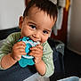 toddler, child, toy, teething_toy, indoor, playpen, smiling, cute, baby, person, clothing, hands, face, young_child, happy, chewing, closeup, furniture, room, casual