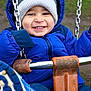 blue_jacket, chains, child, cold_weather, cute, face, fun, gloves, happy, jacket, knit_hat, outdoor, park, person, playground, seat, smiling, swing, toddler, winter